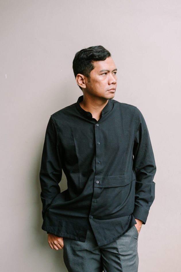 Thoughtful asian man poses in minimalist style clothing against a neutral backdrop looking away with a pensive expression